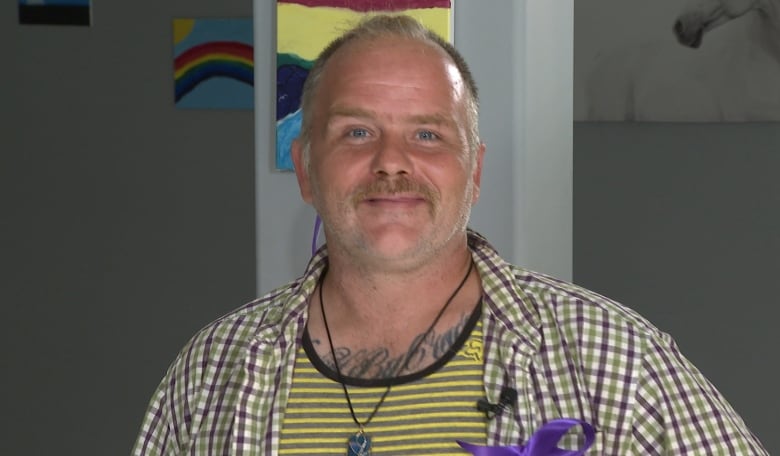 Man in yellow stripped shirt and a purple ribbon on chest