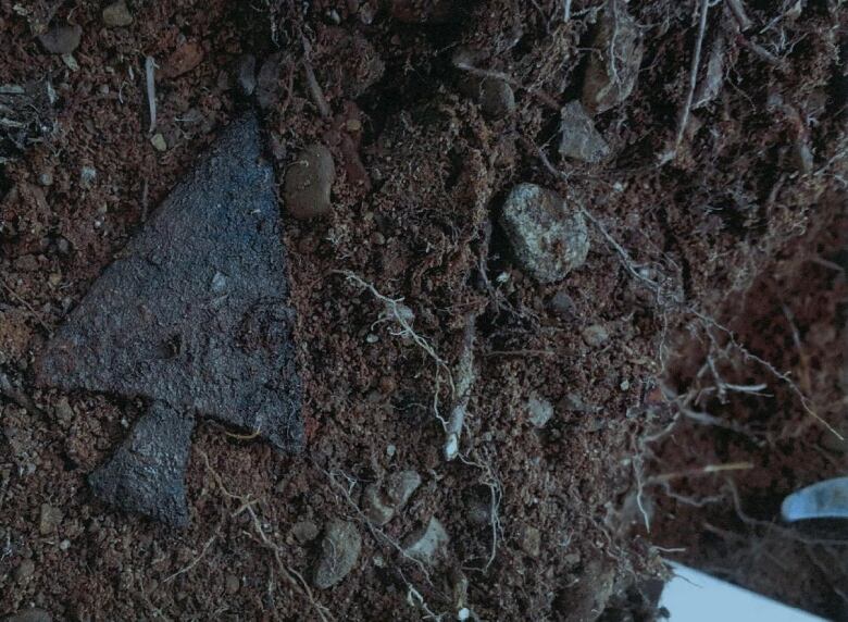 A black triangular harpoon tip laying in dirt.