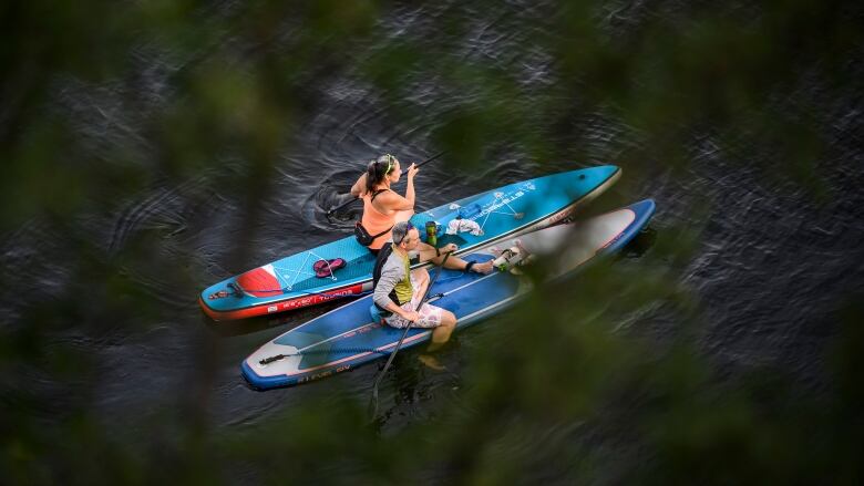 Two people sit on paddleboards on a river in summer.