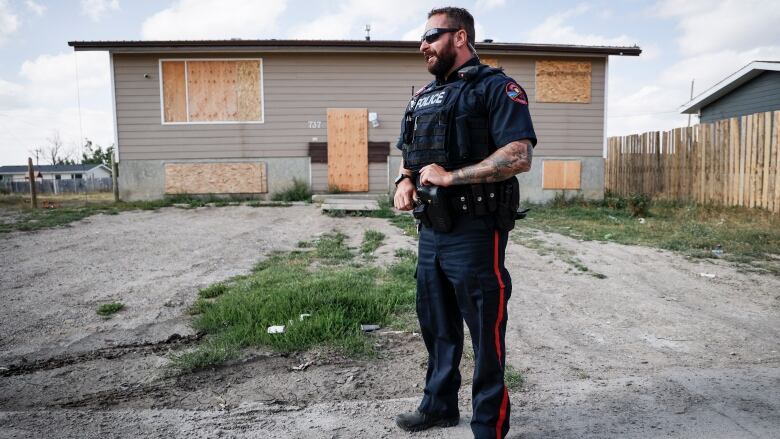 a man in a blue police officer's uniform stands outside in front of a boarded up house. 