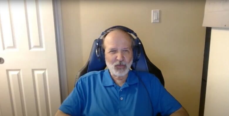 A man sits wearing a blue shirt and headphones.