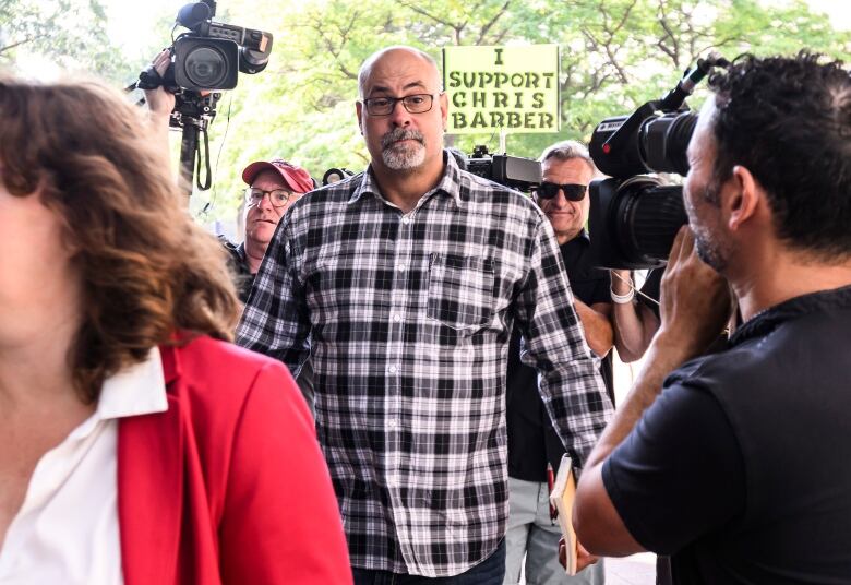 A man in a plaid shirt and glasses walks toward a courthouse on a summer morning.