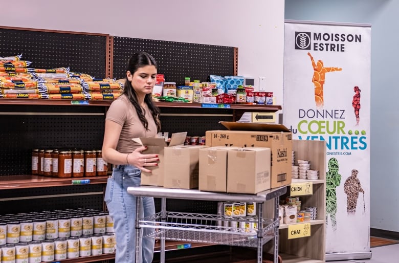 A woman unpacking boxes of food in order to replenish shelves at a food assistance store.