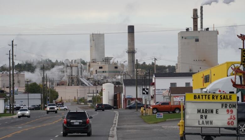 Cars drive on a street leading to a large industrial plant 