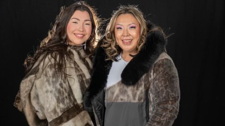 Two Inuit women dressed in seal skin smile at the camera.