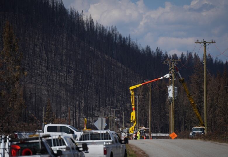 A large yellow vehicle with a long arm repairs a power pole.