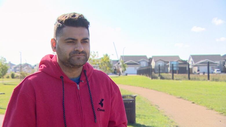 A man can be seen wearing a red jacket, standing in a park. 