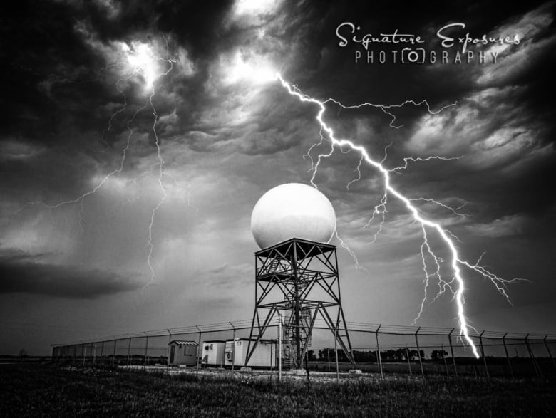 Lightening strikes against a dark sky, with a white weather radar ball in the foreground.