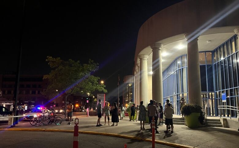 A police car with flashing lights and a crowd outside a large building with pillars at night.