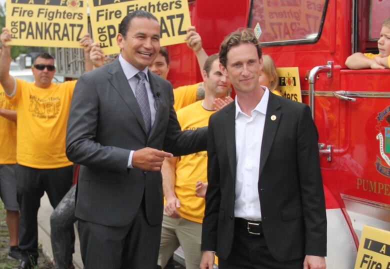 Two people smile for the camera, while people in yellow shirts celebrate in the background. 