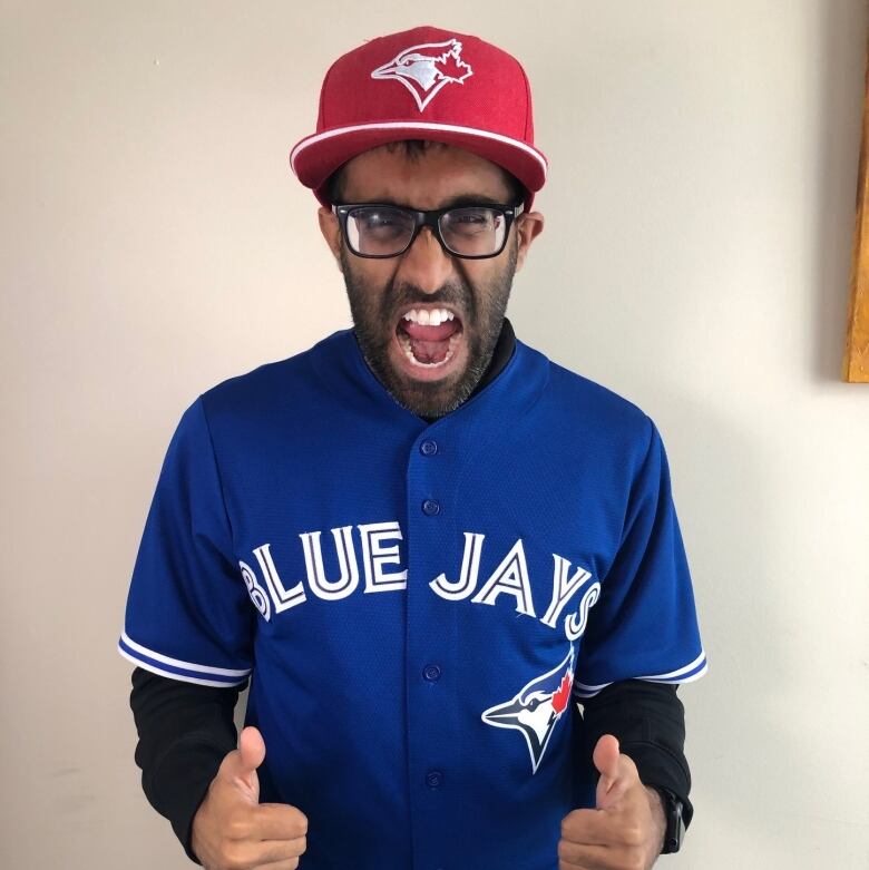 Man wearing Toronto Blue Jays jersey flashes two thumbs up at the camera.