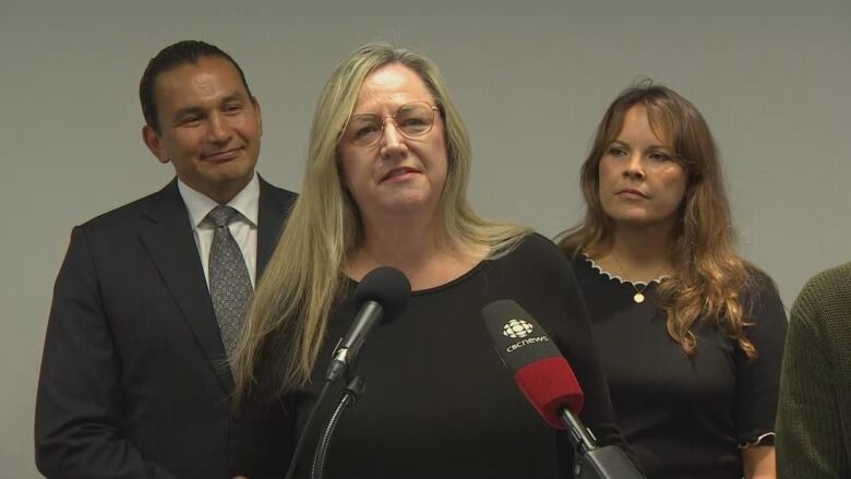 A woman in a black sweater speaks to media.