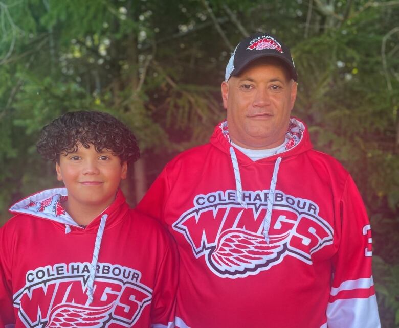 A father and son wearing hockey jerseys pose for the camera.