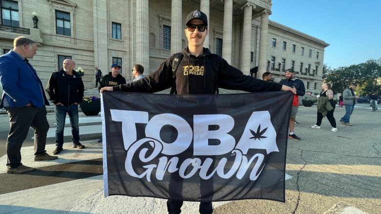 A man wearing sunglasses holds up a flag that says 