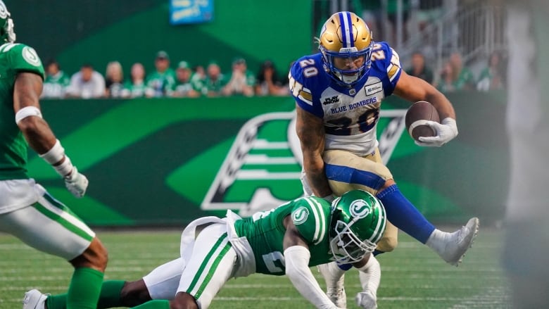 A football player in a white jersey collides with a football player in a green jersey while holding the ball.