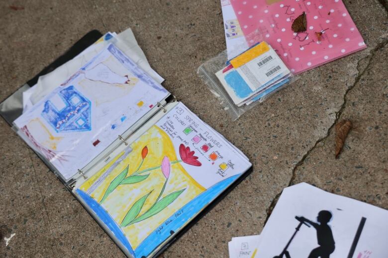 An open binder on a concrete street. Paper in the book shows a drawing of seveeral flowers. 