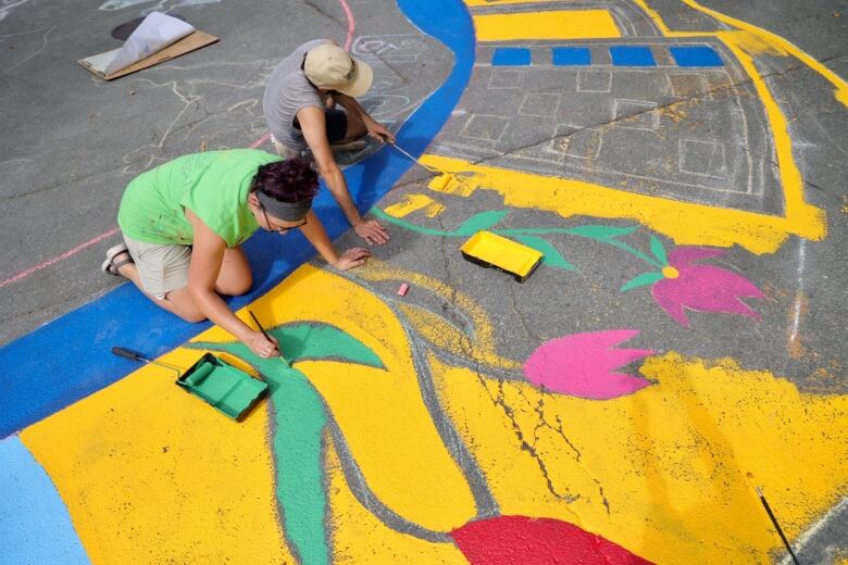 Two people are seen painting flowers on a concrete street.