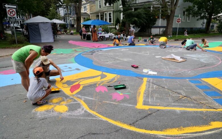 People are seen painting a large, colourful mural on a city street.