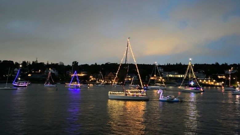 Seven boats strung up with holiday lights.