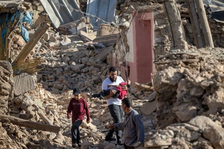 A man carries a young boy while walking in earthquake rubble.