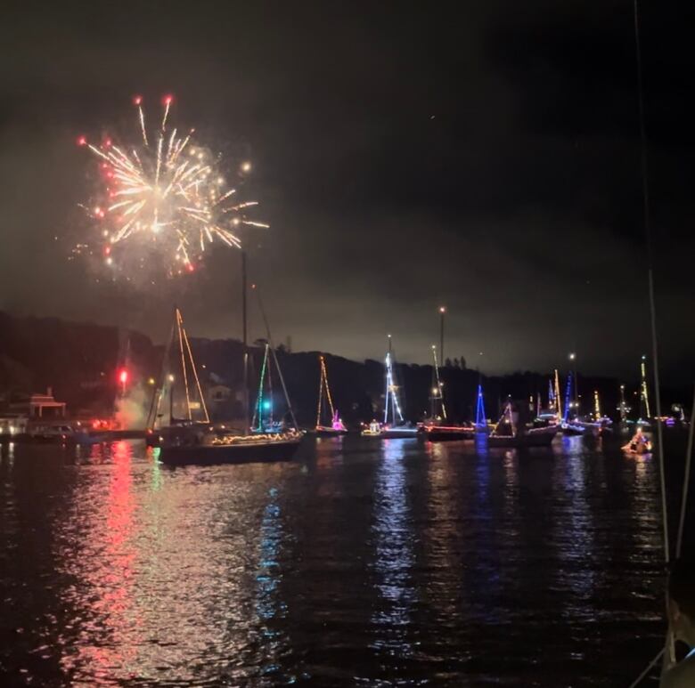 fireworks over the water with boats outlined with string lights sail underneath it.