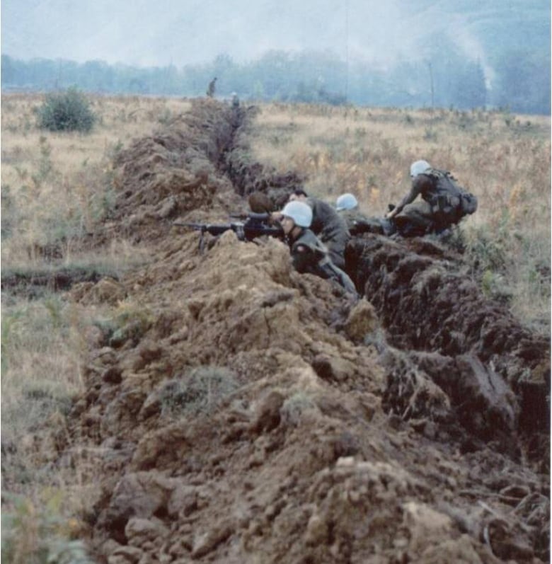 Soldiers crouch down at a trench line.