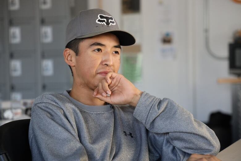 A young man in grey rests his chin on his hand.