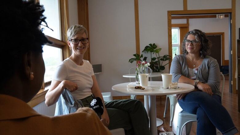 Two women sitting crossed-legged on opposite side of a small white caf table. 