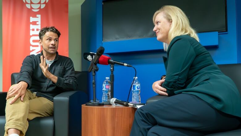 A man and a woman sit across from each other at a desk and speak to each other. 