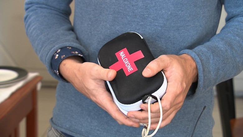 Male hands holding a small black case with a white zipper going around it.