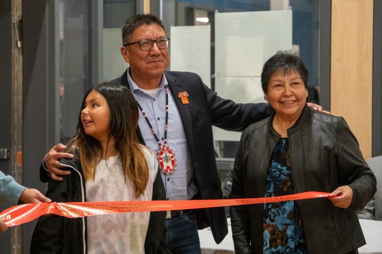 Three people stand together, holding a red ribbon.