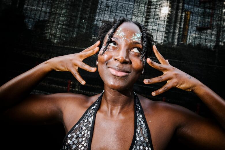 A Black woman wearing a silver top looks away from the camera.