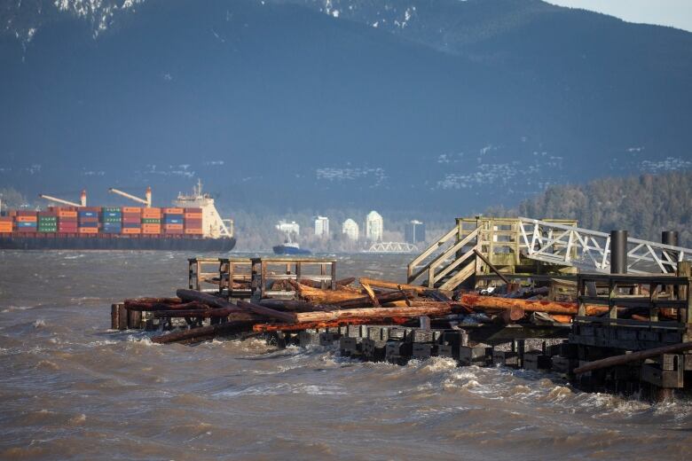 A battered and broken pier is seen overlooking a large container ship and Vancouver's North Shore.