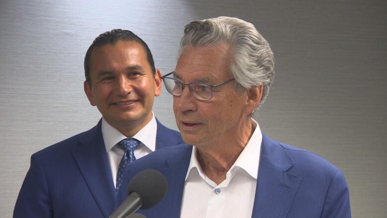 Two politicans in blue suits speak to media.