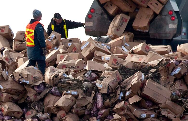 A Canada Food Inspection Agency employee, left, looks on as beef from the XL Foods cattle processing plant is dumped at a landfill site near Brooks, Alta., on Oct. 22, 2012. Lawyers have brokered a tentative deal to settle part of a class-action lawsuit filed over an E. coli outbreak and the largest meat recall in Canadian history.