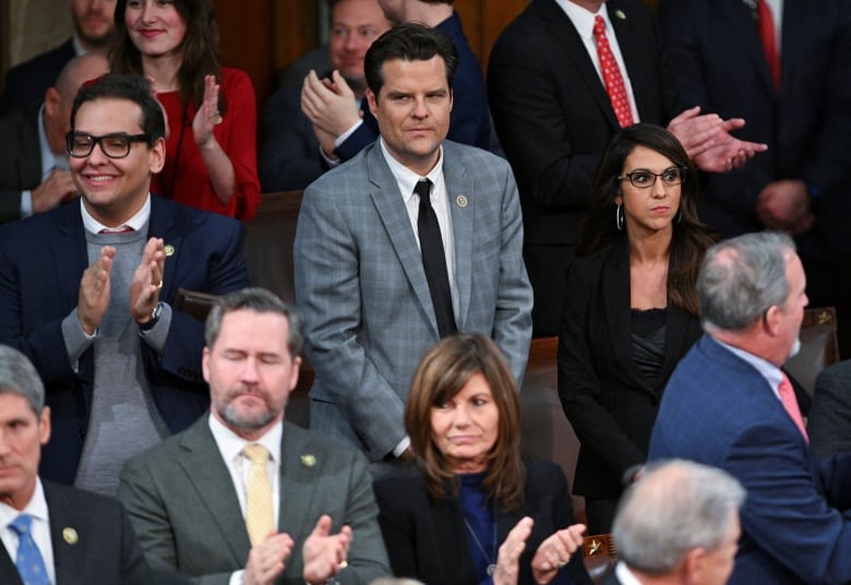 Crowd of lawmakers in House of Representatives, with young man in bright checkered suit in the middle.