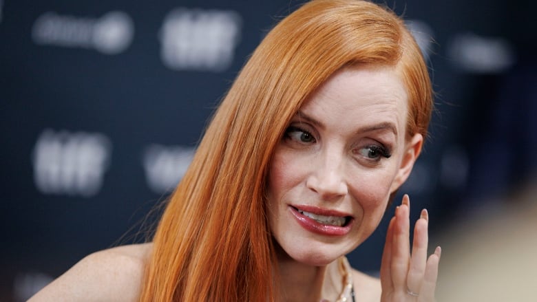 Redhead woman gesturing as if she's whispering into a microphone.