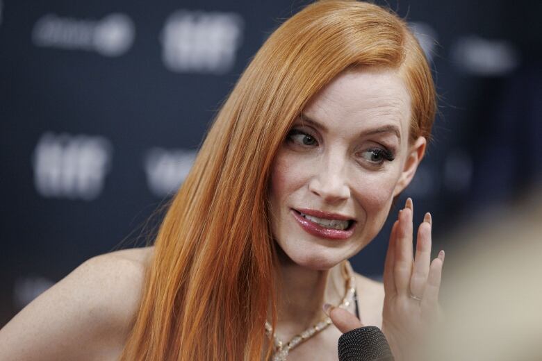 Redhead woman gesturing as if she's whispering into a microphone.