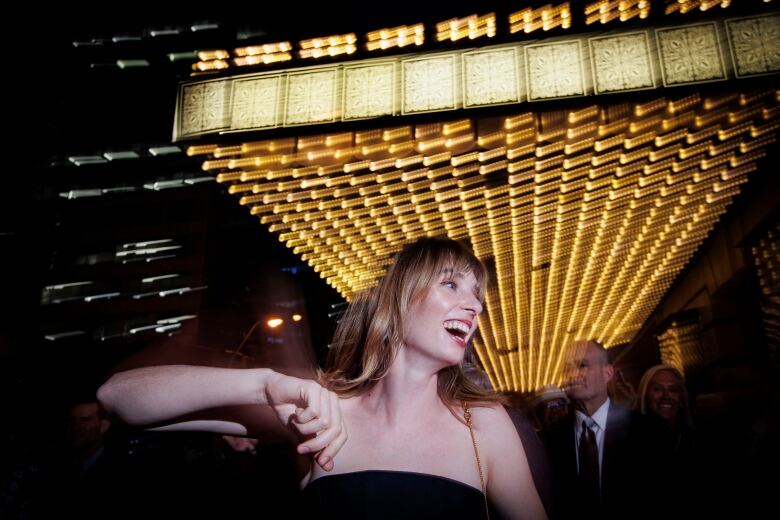 A woman in strapless gown smiles outside a theatre, in an image taken by flash to freeze motion.