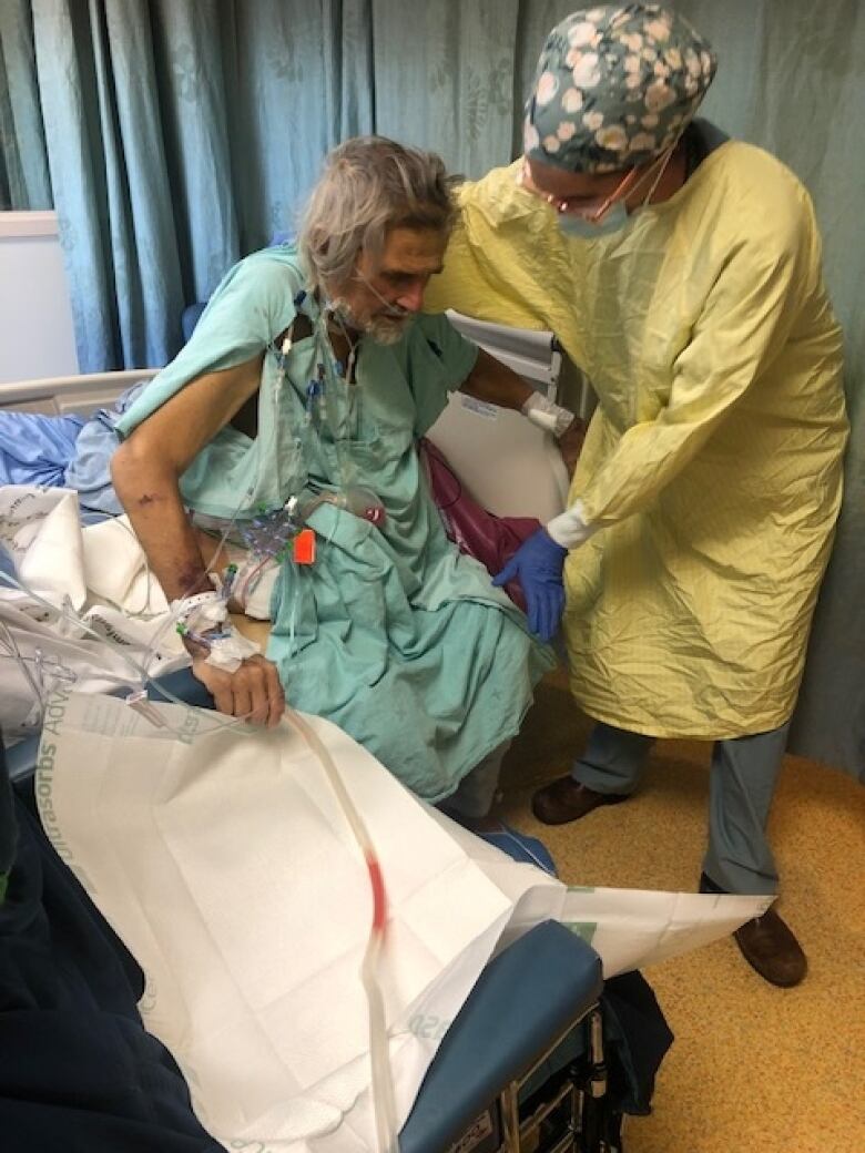 Man receives assistance by a hospital bed.