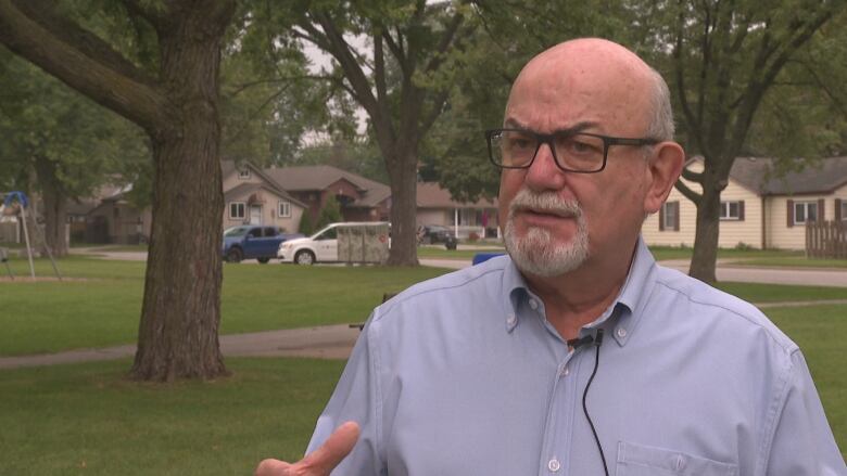 A bespectacled male town mayor speaks in a park among trees.