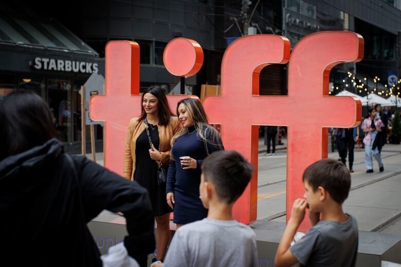 Two women pose in front of the TIFF logo in bold red letters.