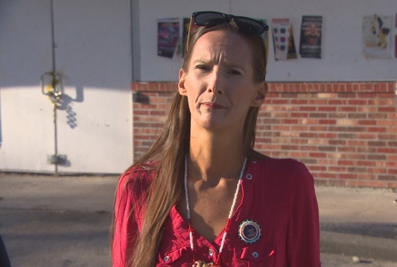 A woman wearing a red shirt stands in front of a building.