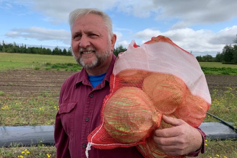 Man is standing in a farming field holding a bag of cabbages.