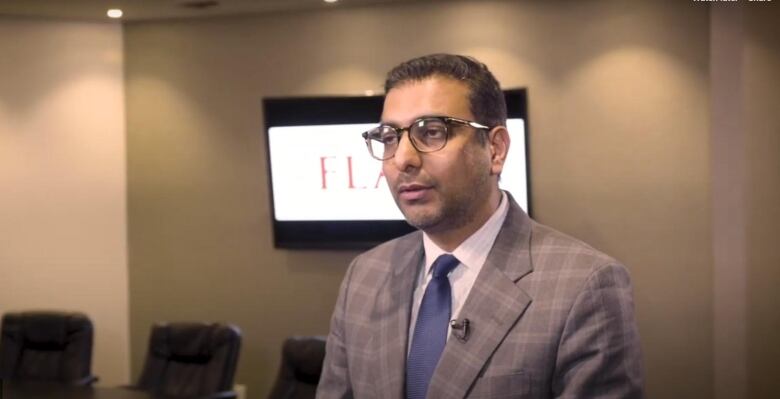 A man in a suit speaks to the camera in a board room.