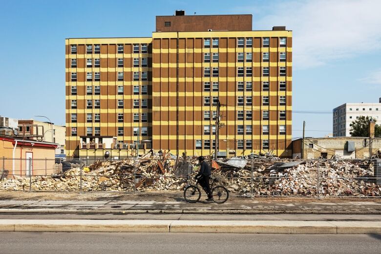 A cyclist rides by a pile of rubble in a city downtown.