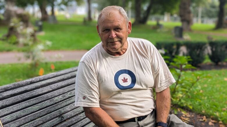 A man with an air force shirt sits on a bench in a cemetery 