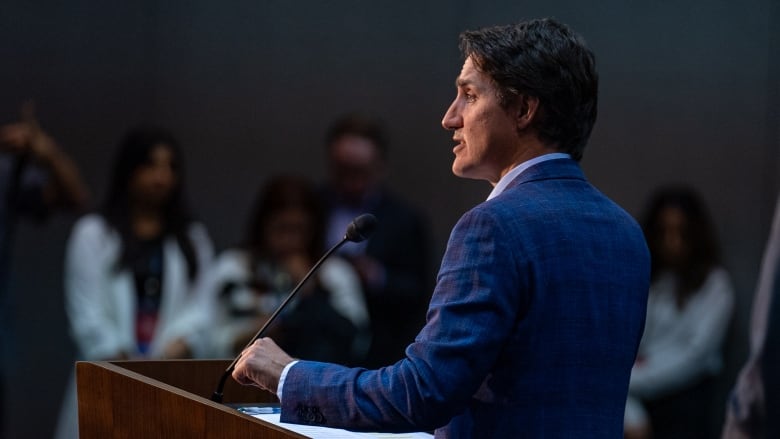 A man in a blue suit speaks at a podium.