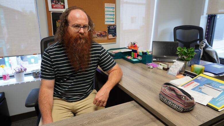 A man with glasses and a beard sits at a desk.