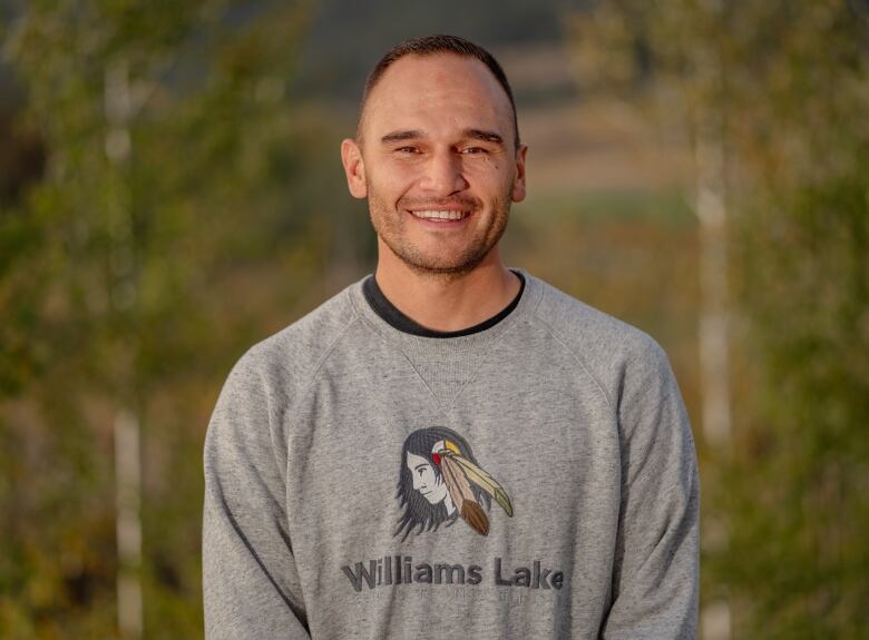 A smiling Indigenous man wearing a grey sweater.